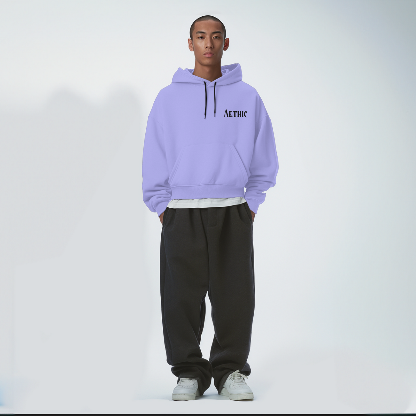Person wearing a light lavender hoodie with text and dark pants on a white background
