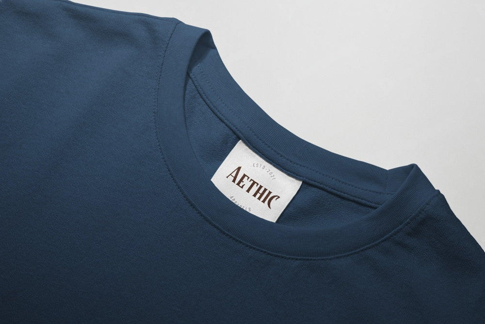 Close-up of a navy blue t-shirt with a white label displaying 'AETHIC' on a light gray background.