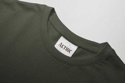Close-up of a green t-shirt with a 'AETHIC' label on a gray background