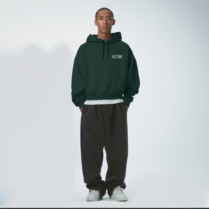 Person wearing a Bottle green hoodie and dark pants on a white background
