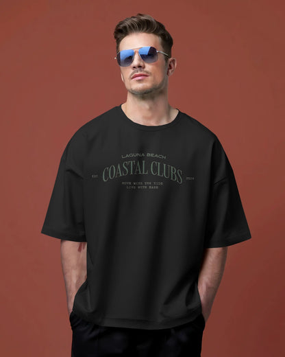 Man wearing a Colour_black 'Coastal Clubs' t-shirt against a brown background
