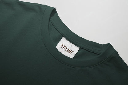 Close-up of a green t-shirt with 'AETHIC' label on a gray background