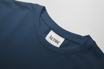 Close-up of a navy blue t-shirt with a white label displaying 'AETHIC' on a light gray background.
